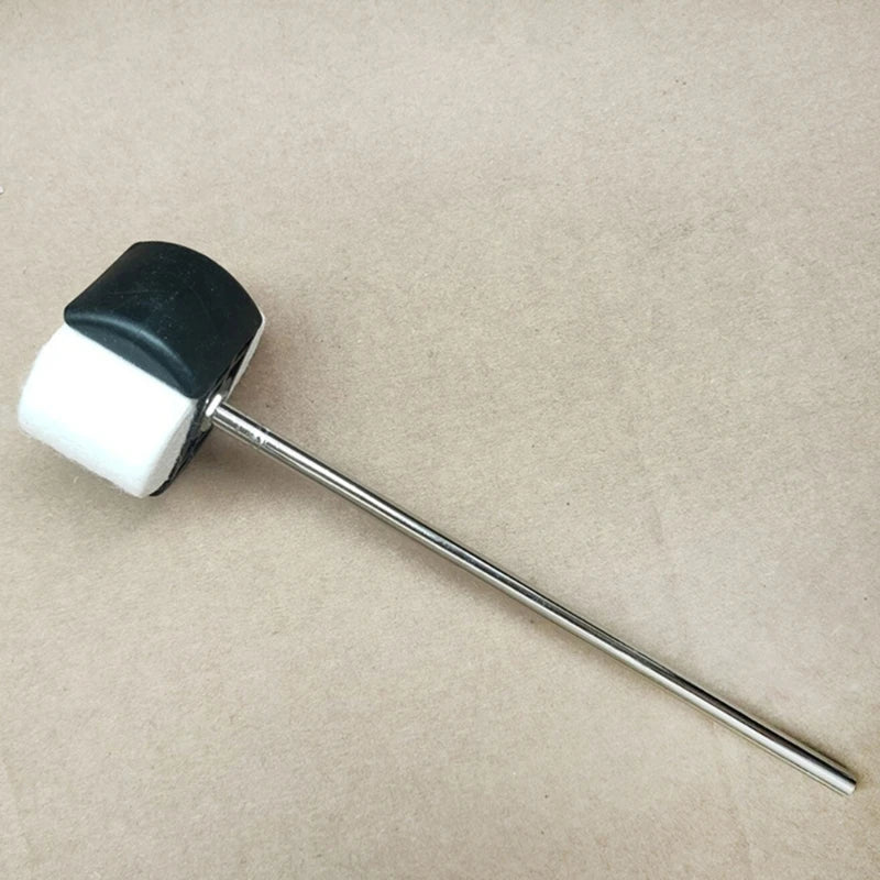 A silver bass drum pedal beater with felt and rubber heads resting on brown paper.