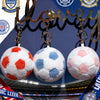 Three soft stuffed soccer ball toys hanging from a gold chain against a dark blue background.