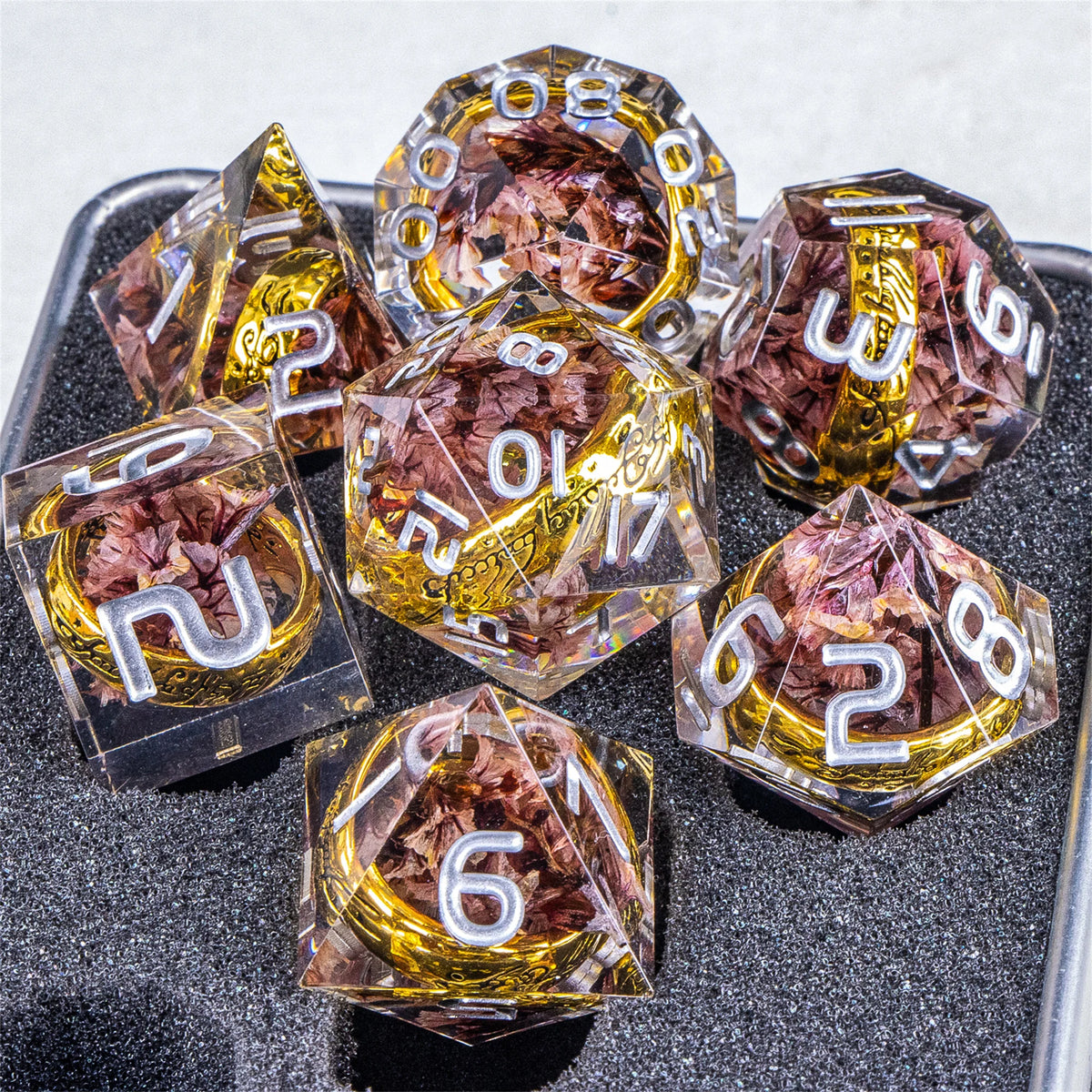 A collection of translucent resin dice with golden elven numbers and reddish-brown inclusions resting on a dark surface.
