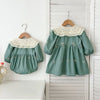 A mint green girls' party dress with lace trim and embroidered details hanging on a white wooden rack.