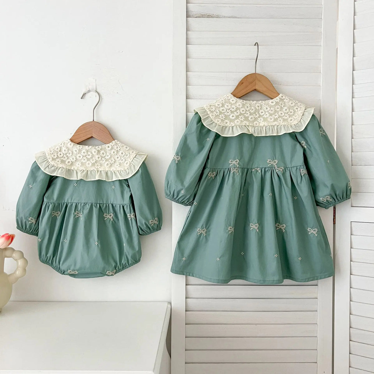 A mint green girls' party dress with lace trim and embroidered details hanging on a white wooden rack.