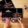 A hand is painting a scratch art scene featuring a Japanese pagoda and Mount Fuji against a night sky background.