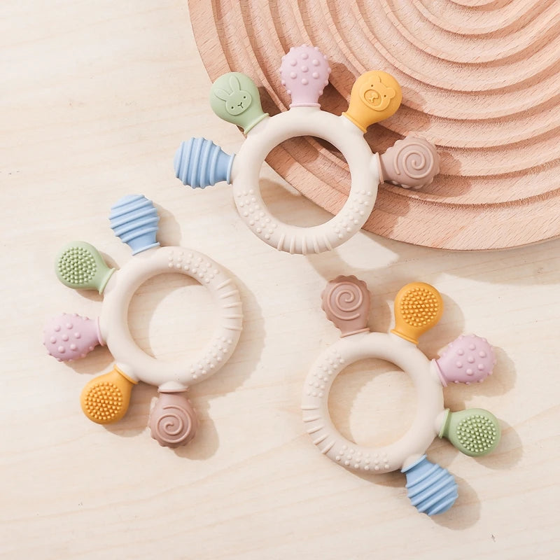 Set aus Silikon-Schnullerringen in Pastellfarben (rosa, gelb, grün, blau) auf Holz