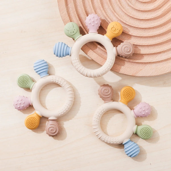 A set of silicone teether rings in various pastel colors, including pink, yellow, green, and blue, resting on a wooden surfac