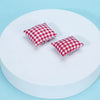 Two red and white checkered mini pillows displayed on a white circular surface.