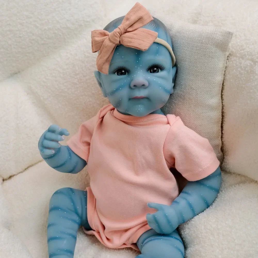 A lifelike reborn baby doll with blue skin and pink clothing is resting on a white fluffy surface.