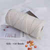 A roll of natural cream-colored cotton macrame rope with loose beads displayed on white paper.