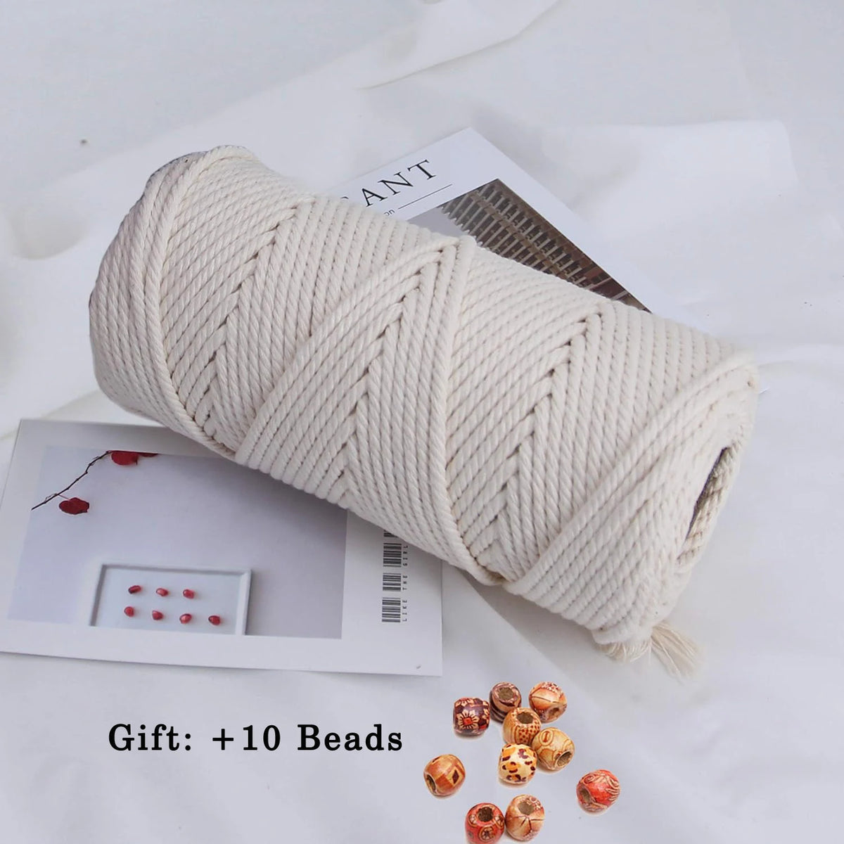A roll of natural cream-colored cotton macrame rope with loose beads displayed on white paper.