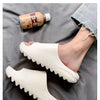 A pair of white EVA platform slides shown next to a bottle of oil on a dark gray fabric.