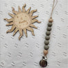 A wooden sun-shaped bead pacifier clip with a silicone teether on a leather cord.