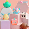 A collection of cute, colorful geometric monster vinyl figures in various pastel shades displayed on white and pink pedestals
