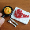 A miniature dollhouse set featuring a beef steak and pasta food item on a white napkin with a fork.