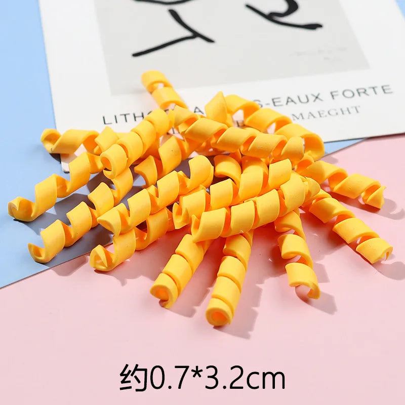 A pile of bright yellow polymer clay marshmallow charms for DIY crafts is displayed on a pink surface.