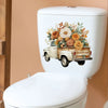 A white toilet tank features a floral truck wall sticker depicting an old pickup truck loaded with colorful flowers.