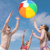 Three people are throwing a rainbow inflatable beach ball high into the air against a blue sky.