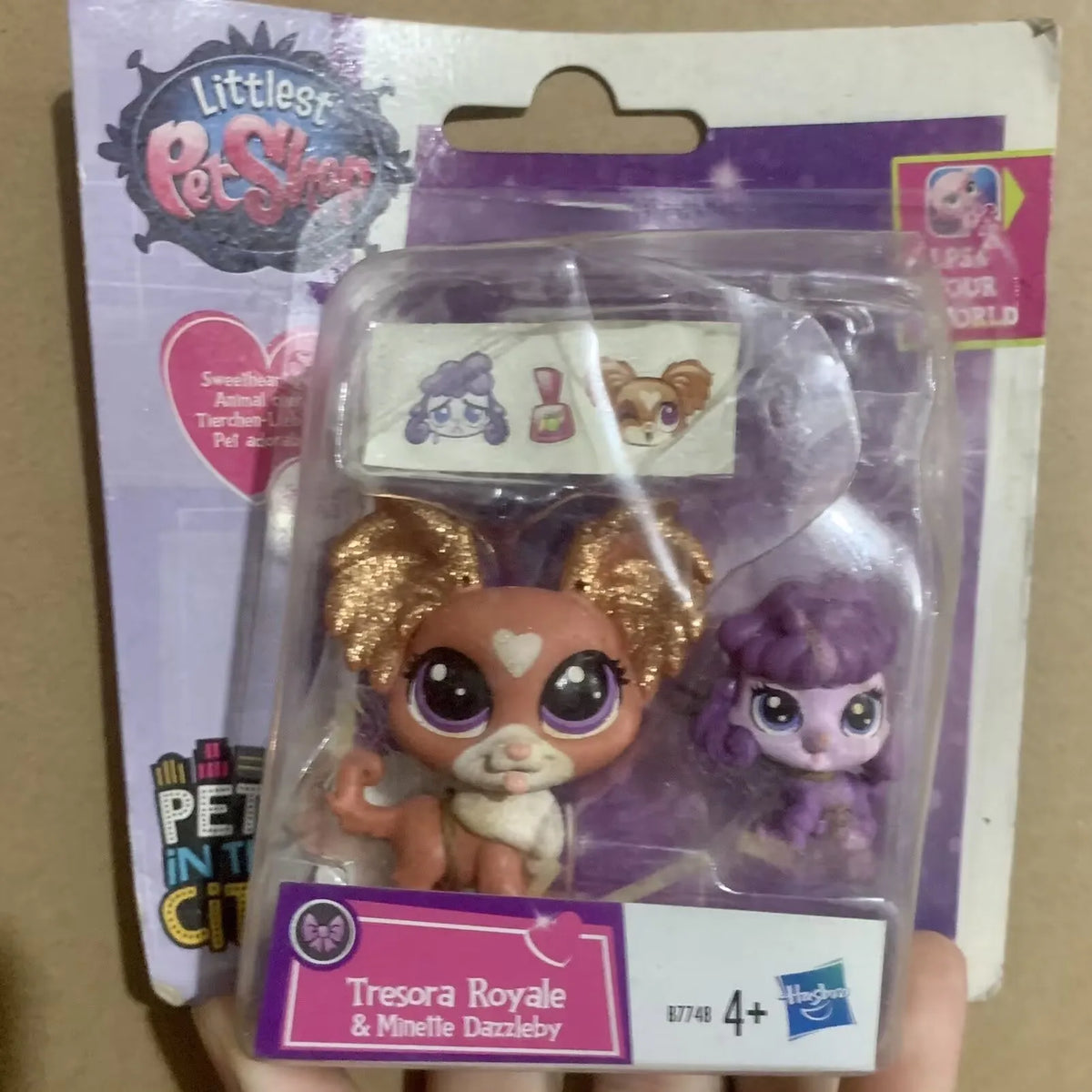 A clear plastic package containing three small animal figures, including a brown and white creature and a purple figure.