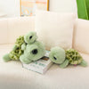 A soft green and yellow patterned tortoise plush pillow resting on a white sofa cushion.