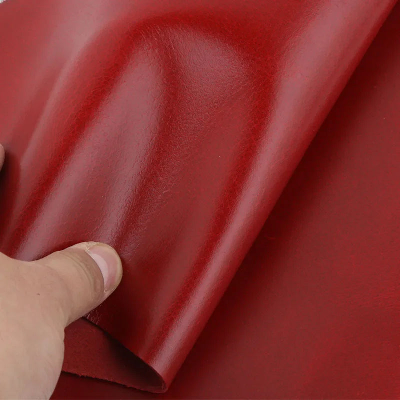 A close-up view of a smooth, wine red oil wax leather sheet being held and folded.