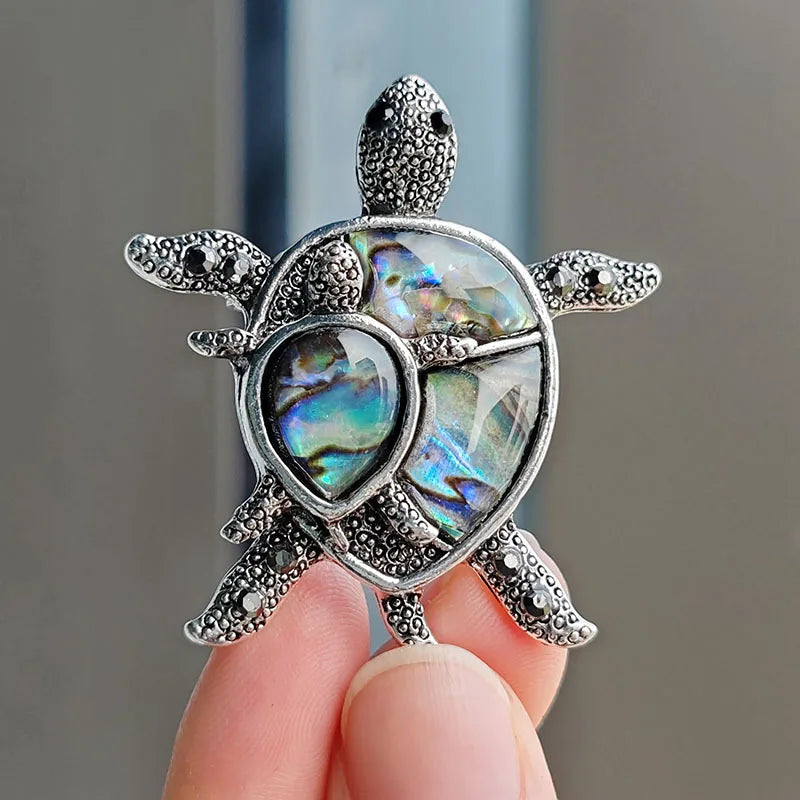 Silver rhinestone turtle brooch pin with iridescent shell detail being held by a hand