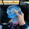 A hand holds a translucent blue jellyfish squish toy with a name written on it inside a car interior.