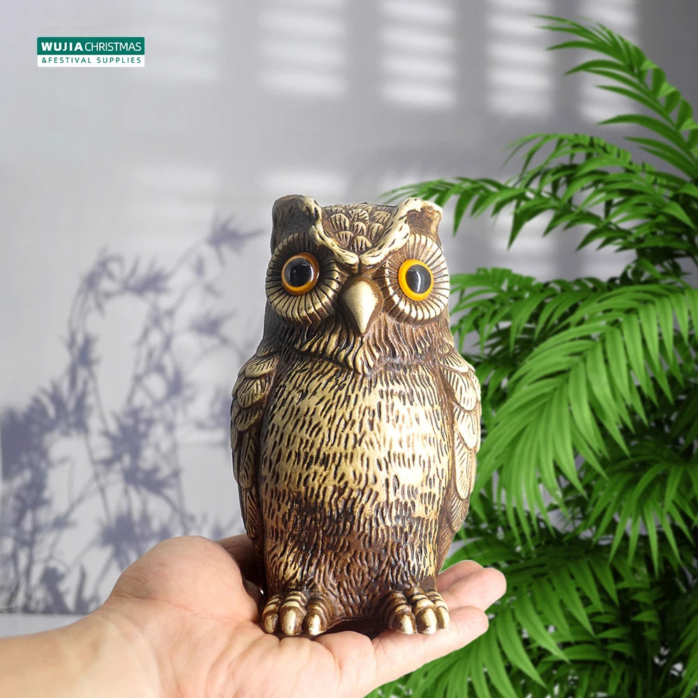 A realistic owl garden statue is held in a hand, featuring brown and tan feathers and large yellow eyes.