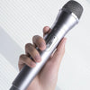 A hand holds a silver microphone with a mesh grille, used as a prop for kids' performances.