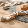 A wooden train set with numbered cars is placed on a textured rug next to draped fabric.