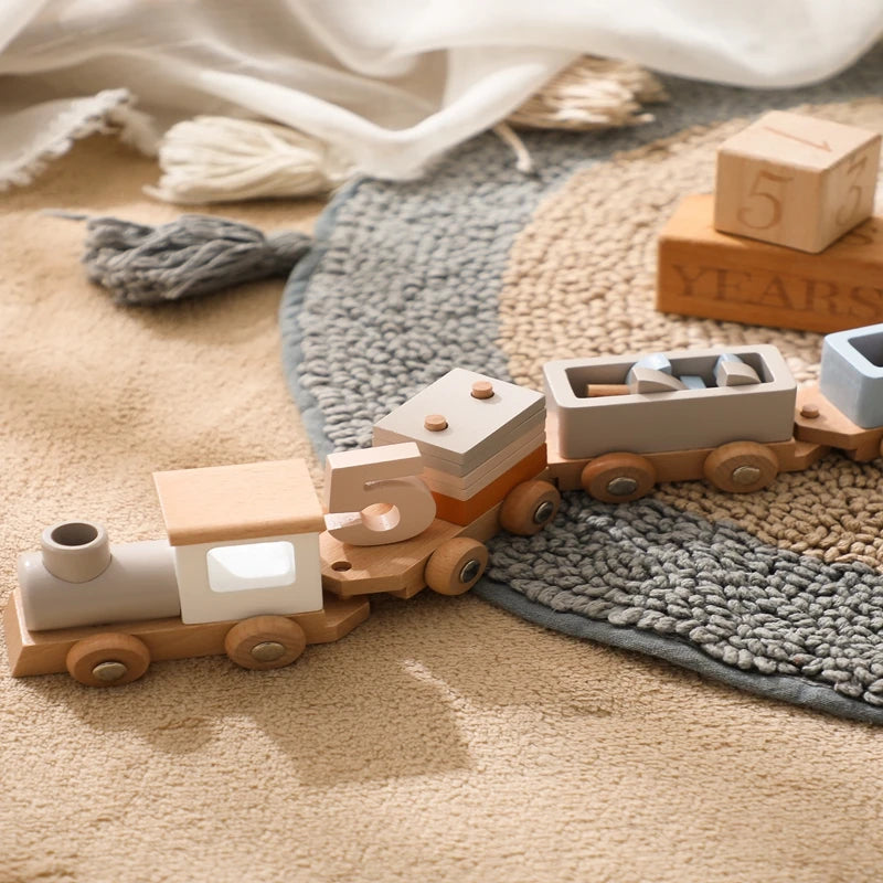 A wooden train set with numbered cars is placed on a textured rug next to draped fabric.