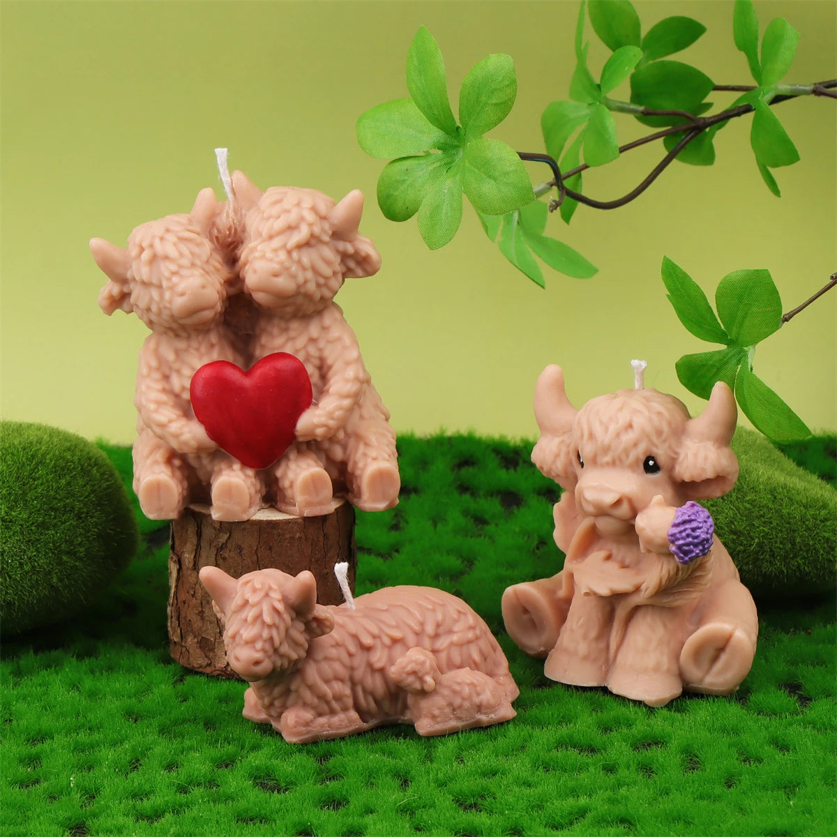 A set of four silicone candle molds shaped like Highland cows in various poses and colors on green moss.
