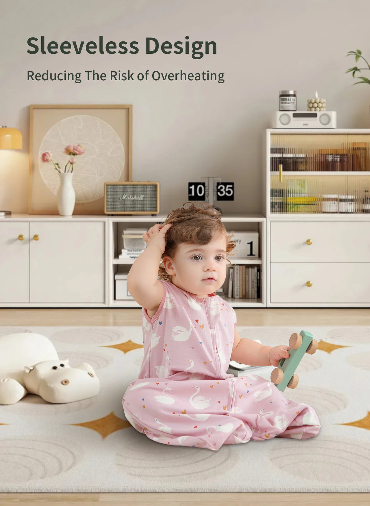 A baby wearing a pink sleeveless sleeping bag is sitting on a rug in a bright room.
