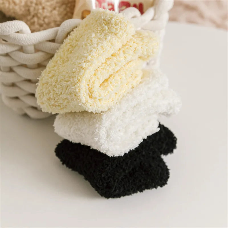 Three pairs of baby anti-slip fleece socks in yellow, white, and black stacked in a woven basket.