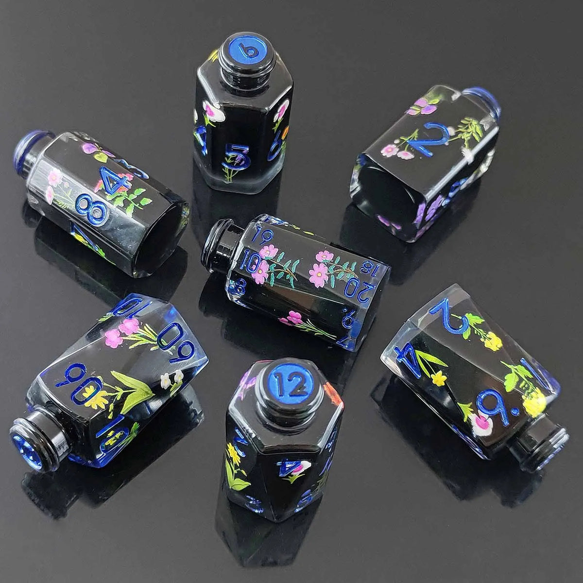 A set of seven floral resin potion bottle polyhedral dice displayed on a dark surface.