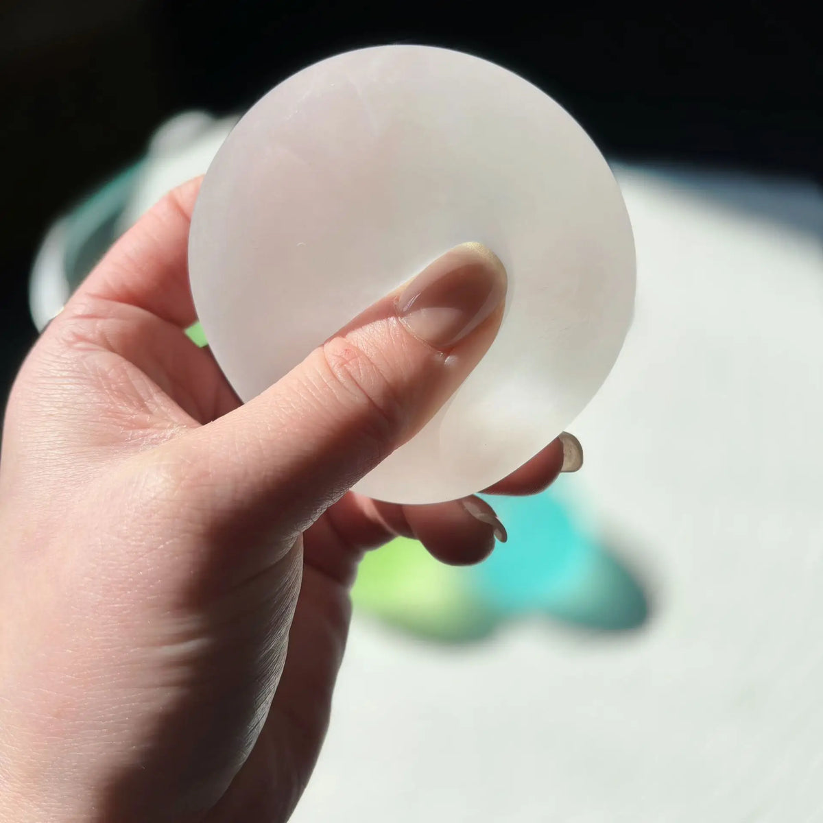 A hand holds a translucent, oval-shaped squishy stress cube for sensory play.