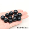 A hand holds several smooth black obsidian crystal spheres.