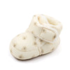 A pair of cream-colored baby winter snow boots with fuzzy ball accents.
