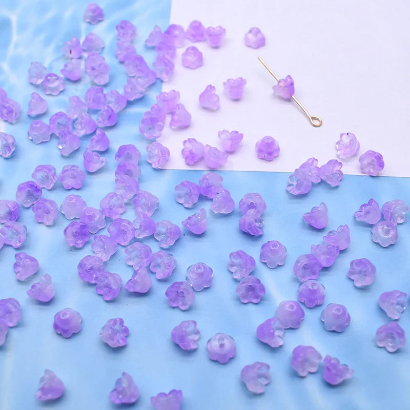 A collection of small purple glass beads shaped like lily of the valley flowers scattered on a white background.