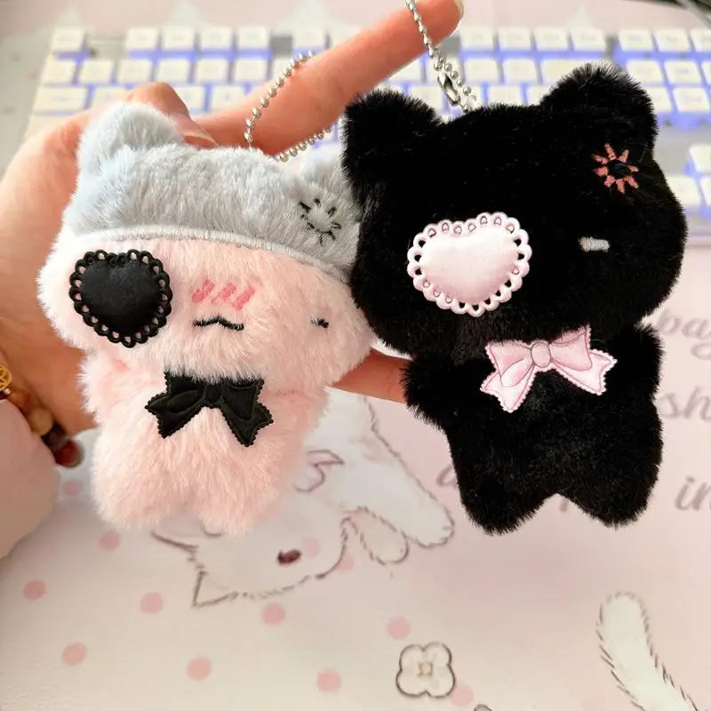 A pair of soft pink and black plush cat keychains are held by a hand against a white background.