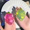 A hand holds a translucent, squishy grape-shaped fidget toy with multiple colors including pink, green, and yellow.