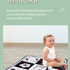 A baby is playing on a black and white mesh fabric activity mat with various toys.