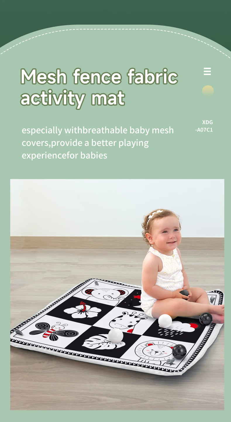 A baby is playing on a black and white mesh fabric activity mat with various toys.