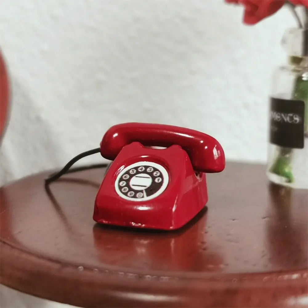 A vintage red rotary telephone miniature sits on a wooden surface next to a glass bottle.