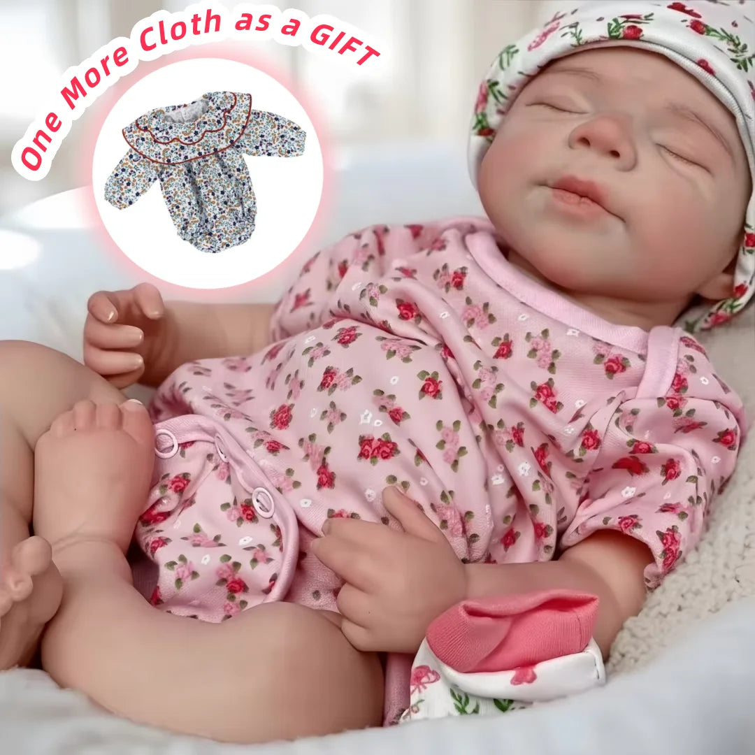 A lifelike silicone reborn baby doll wearing a pink floral outfit is shown resting on white fabric.