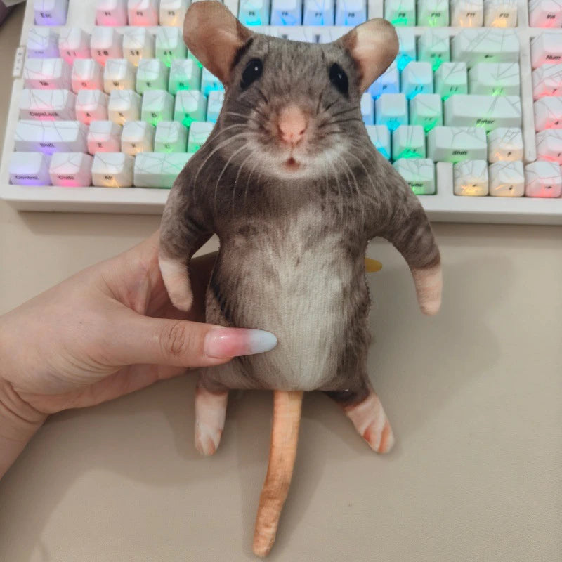A realistic gray and white rat plush toy with large ears and a long tail is held above a keyboard.