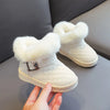 A pair of white girls' snow boots with crystal bowknot details and plush white lining being held by a hand.