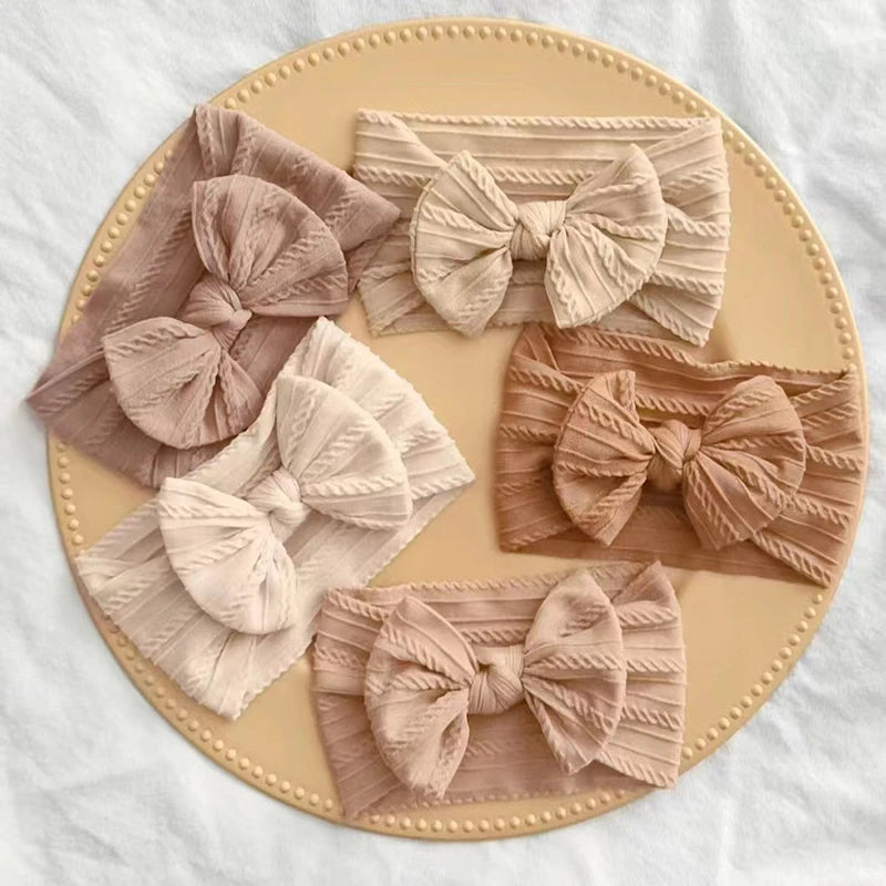 A set of three soft stretch baby headbands with bows in various shades of beige and pink laid on a round plate.