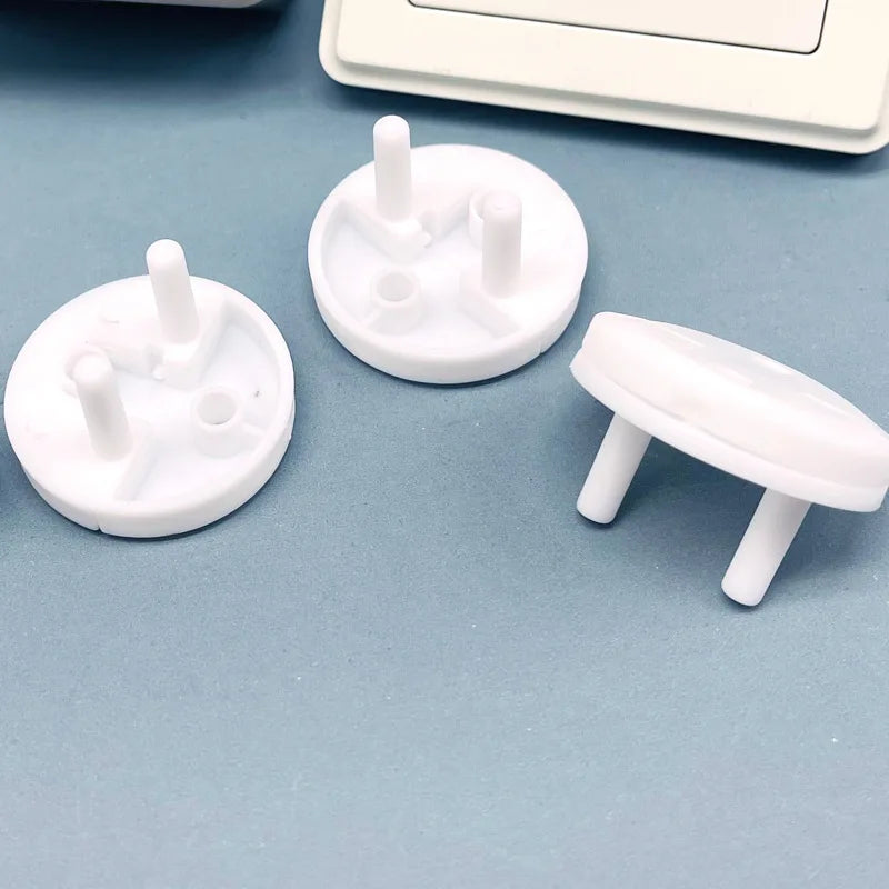 A collection of white rotating socket safety covers for baby proofing are displayed on a light blue surface.