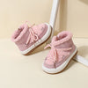 A pair of pink baby winter snow boots with plush lining and white rubber soles resting on a light surface.