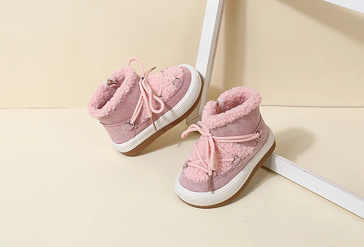 A pair of pink baby winter snow boots with plush lining and white rubber soles resting on a light surface.