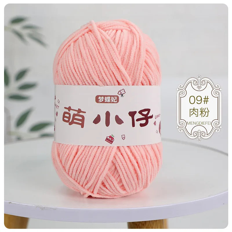 A ball of pink chenille yarn labeled for knitting and crochet is displayed on a white surface.
