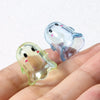 Two translucent acrylic ghost beads, one pale blue and one yellowish-green, are held in a hand.